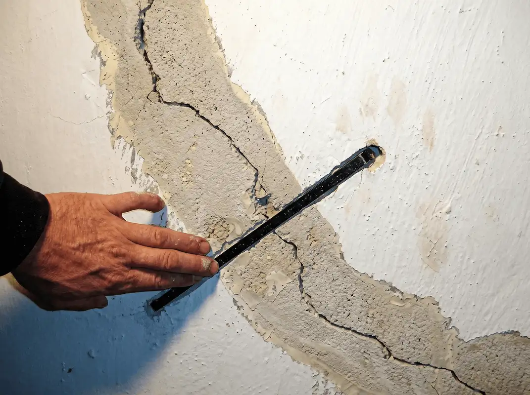 A wall with a large crack is being inspected by a professional in Tucson, AZ